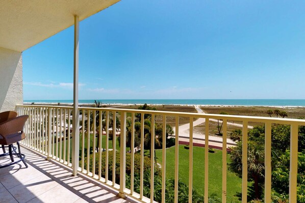 A balcony with a view of a beach and a well-maintained lawn.