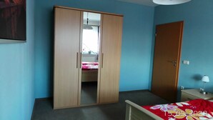 A room with a wooden wardrobe, a bed with a floral bedspread, a bedside table with a lamp, and a door. - Ferienwohnung Reulecke (Blankenburg (Harz))