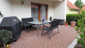 A patio with a table and chairs, a covered grill, and potted plants. - Ferienwohnung Reulecke (Blankenburg (Harz))