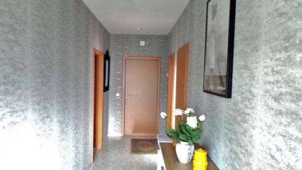 A hallway with textured walls, a wooden door, and a vase with white flowers on a wooden table. - Ferienwohnung Reulecke (Blankenburg (Harz))
