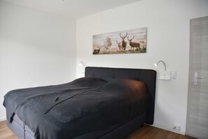 Ein Schlafzimmer mit einem großen Bett, einem Wandbild von Hirschen, Nachttischlampen und einer Tür.