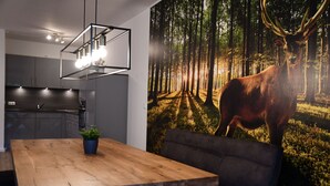 Una cocina moderna con armarios grises, una mesa de comedor de madera con una planta y un mural de un bosque en la pared.