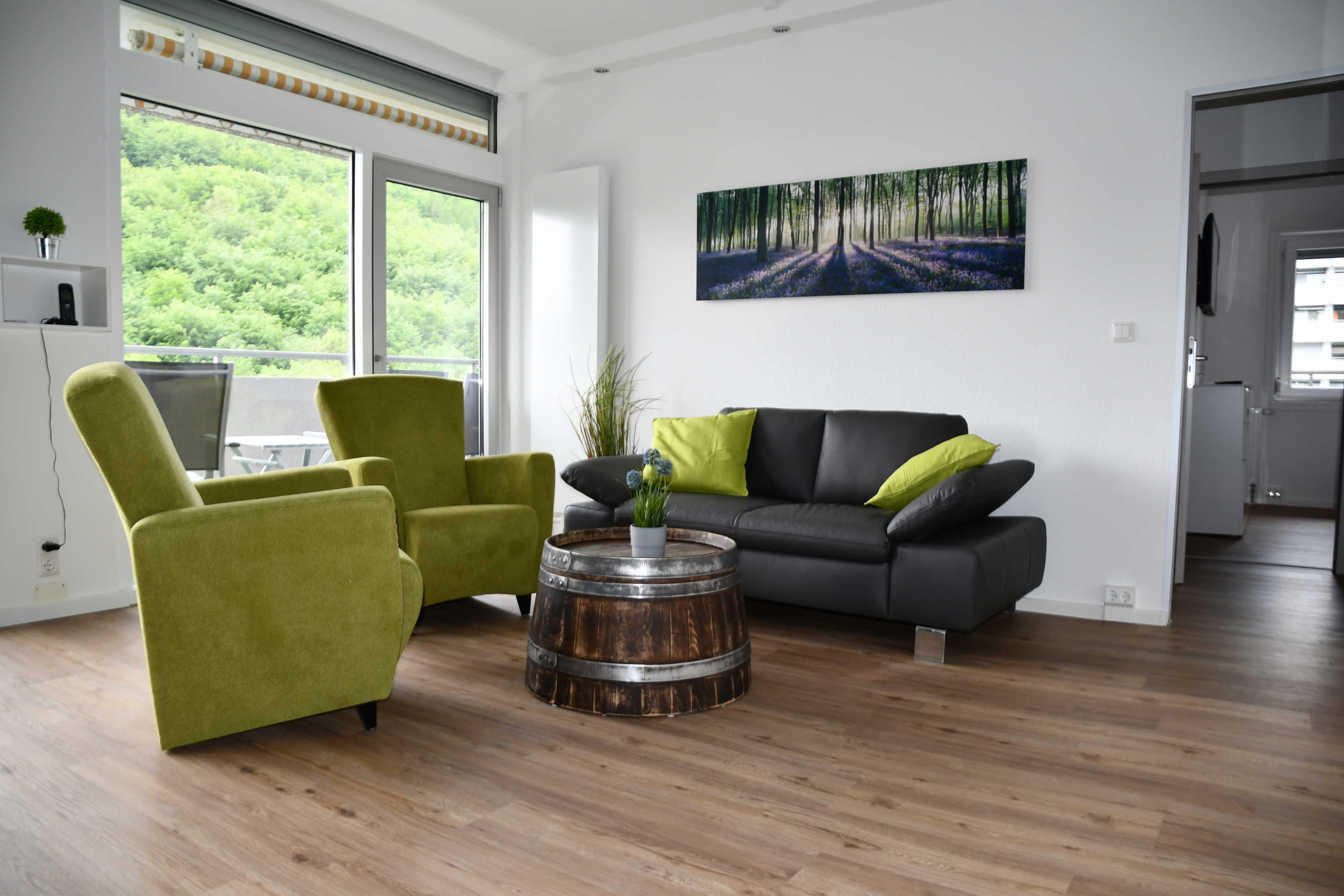 Ein modernes Wohnzimmer mit grauem Sofa, grünen Sesseln und einem Holztisch.