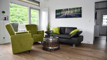 Ein modernes Wohnzimmer mit grauem Sofa, grünen Sesseln und einem Holztisch.