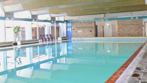 Una piscina interior con agua cristalina, suelo de baldosas y pared de ladrillo al fondo.