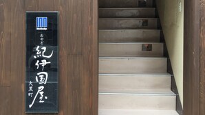 A wooden staircase leading to a room with a sign indicating a room number and a logo. - Oyado Kinokuniya Daikoku Machi (Nagasaki)