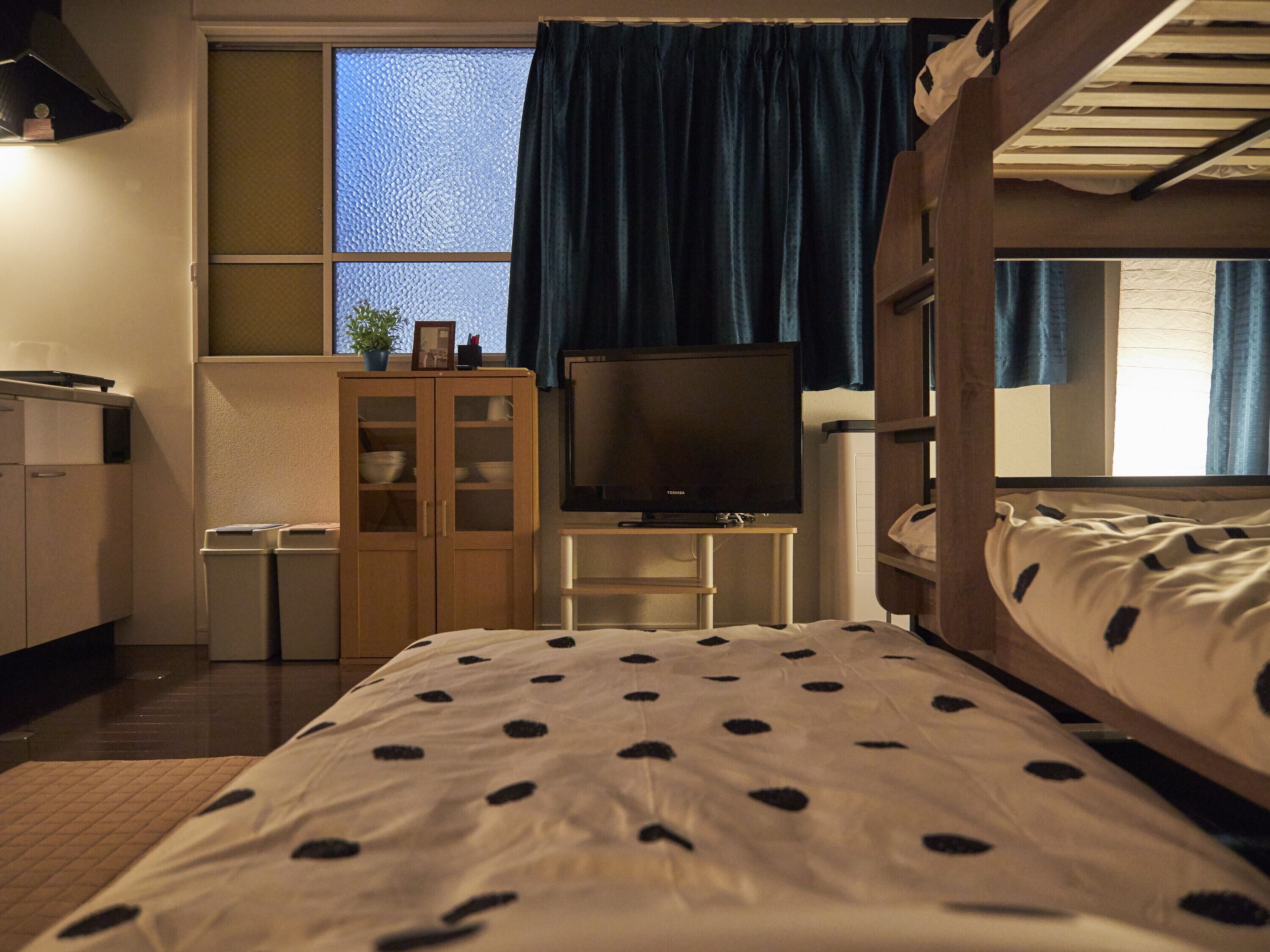 A room with a bunk bed, a desk with a computer, a television, and a window with curtains.