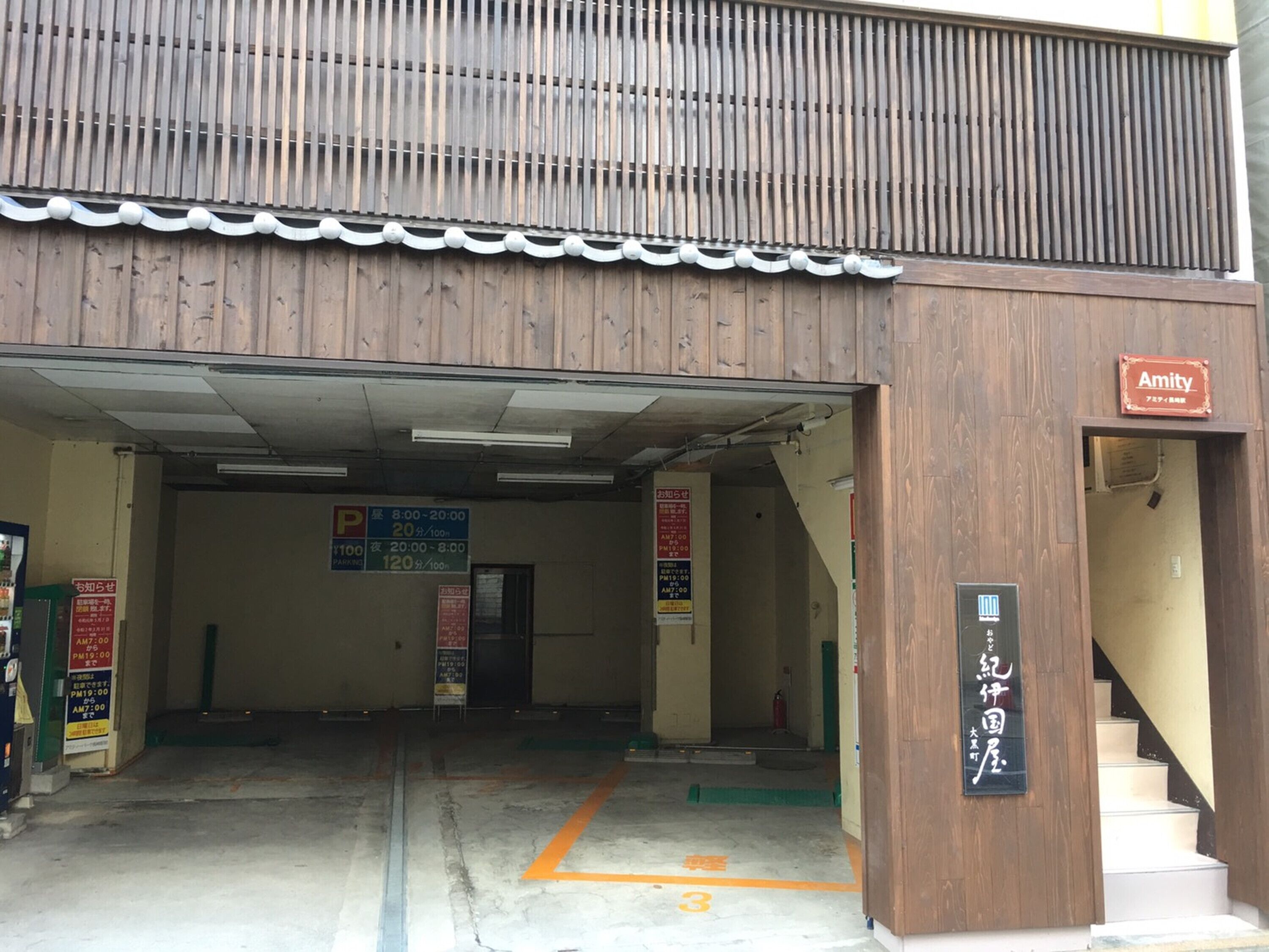 Entrada de un estacionamiento con fachada de madera, un letrero que dice 'Amity' y señalización con tarifas.