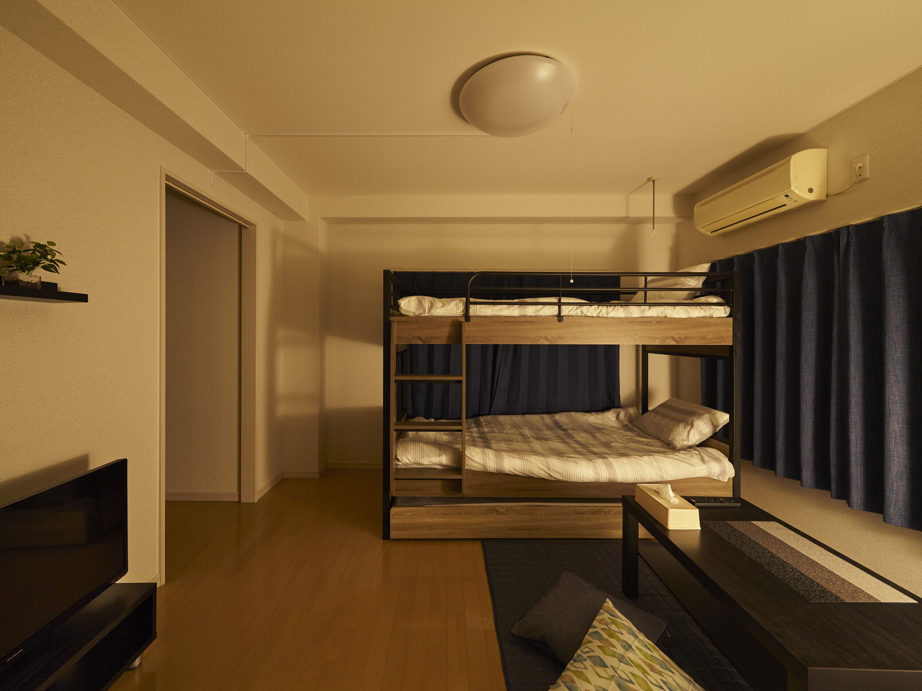 A bunk bed room with a TV, a small table, and a window with curtains.