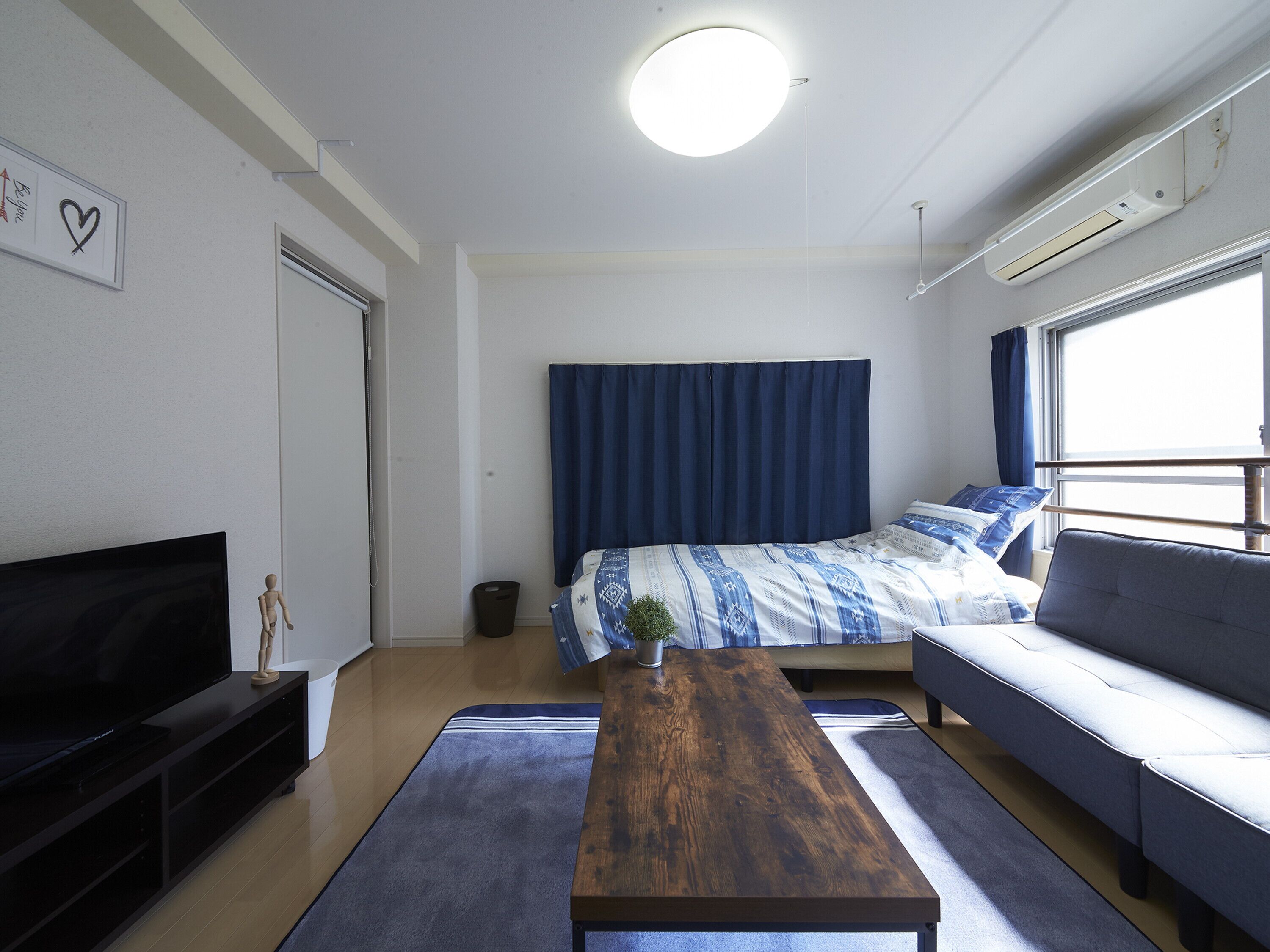 A modern, well-lit room with a bed, sofa, TV, and a small table.