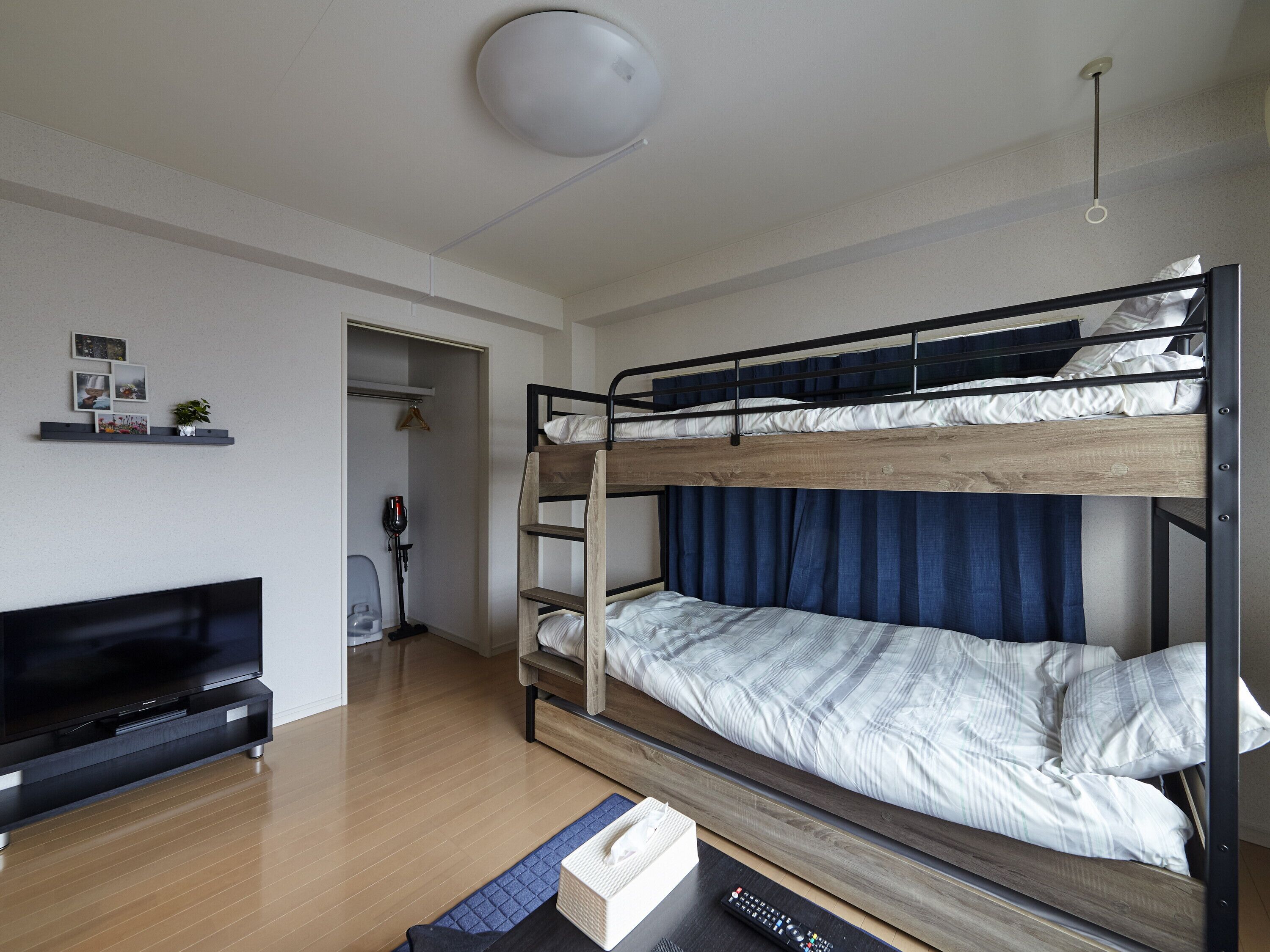 Una cama litera con estructura de madera y cortinas azules, un televisor de pantalla plana y un pequeño estante con fotografías y una planta.