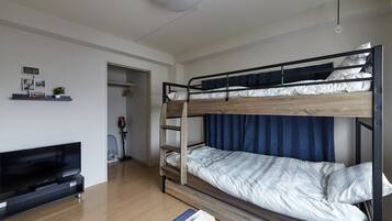 Una cama litera con estructura de madera y cortinas azules, un televisor de pantalla plana y un pequeño estante con fotografías y una planta.