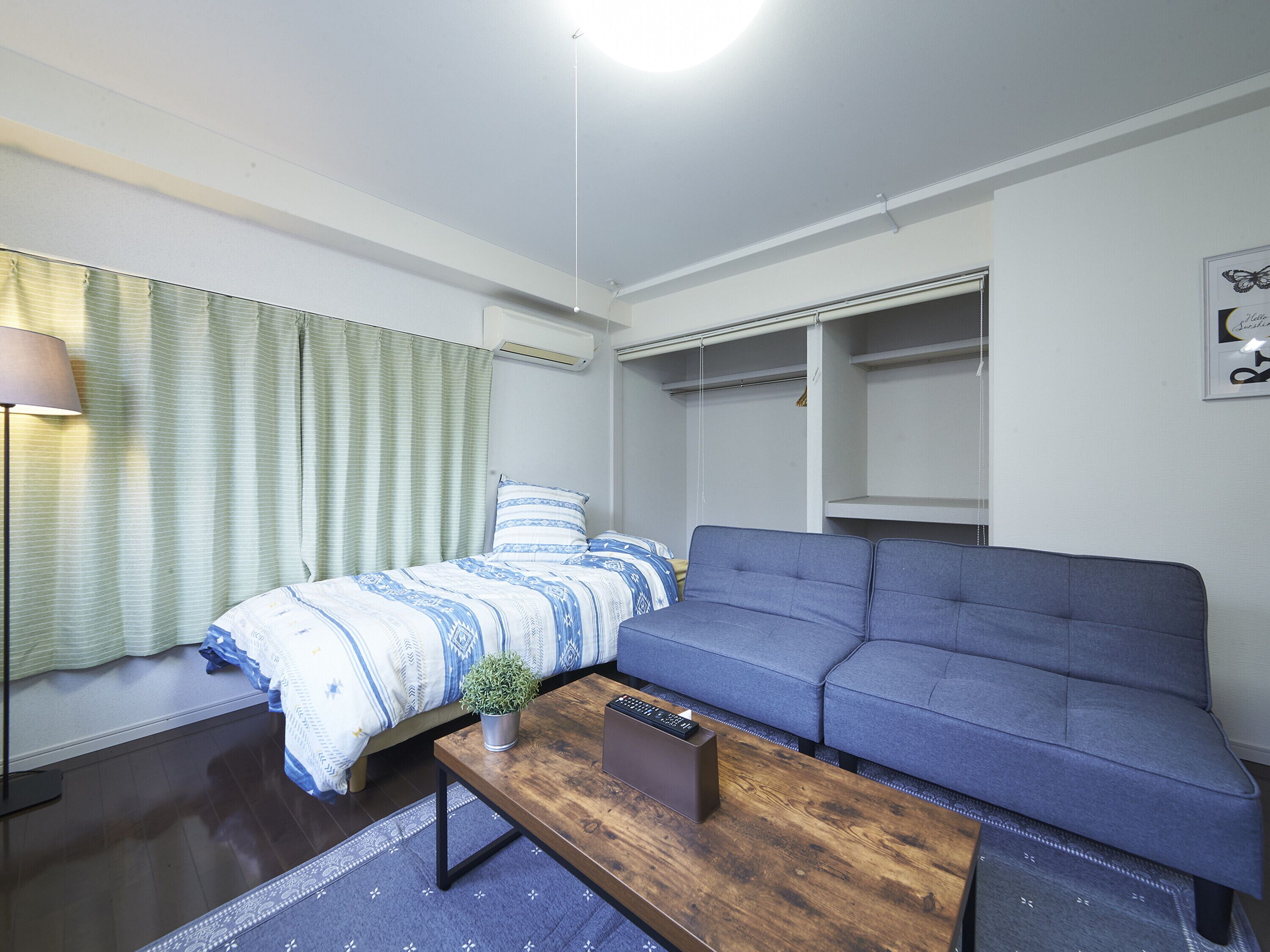 A compact, modern room with a bed, a sofa, a small table, and a wardrobe.