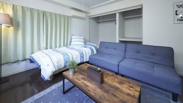 A compact, modern room with a bed, a sofa, a small table, and a wardrobe.