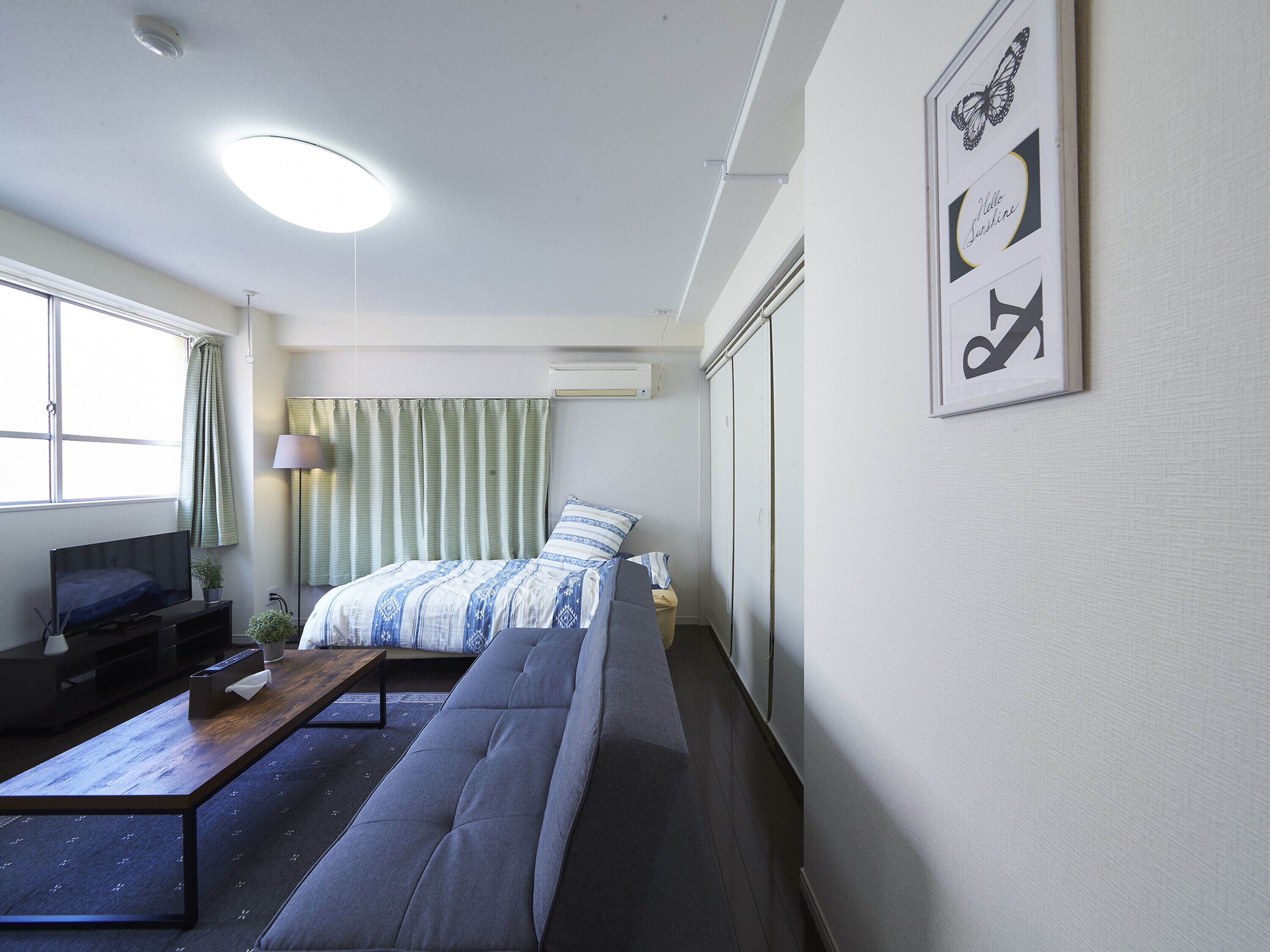 A modern hotel room with a sofa bed, a flat-screen TV, a small table, and a window with curtains.