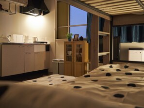 A hotel room with a bed, a small kitchenette, a cabinet, and a window with curtains. - Oyado Kinokuniya Daikoku Machi (Nagasaki)
