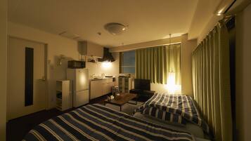 Quarto de hotel com duas camas, uma kitchenette, televisão e janela com cortinas.