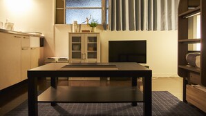 A compact room with a dark wooden table, a small cabinet, a window with curtains, and a fireplace. - Oyado Kinokuniya Daikoku Machi (Nagasaki)