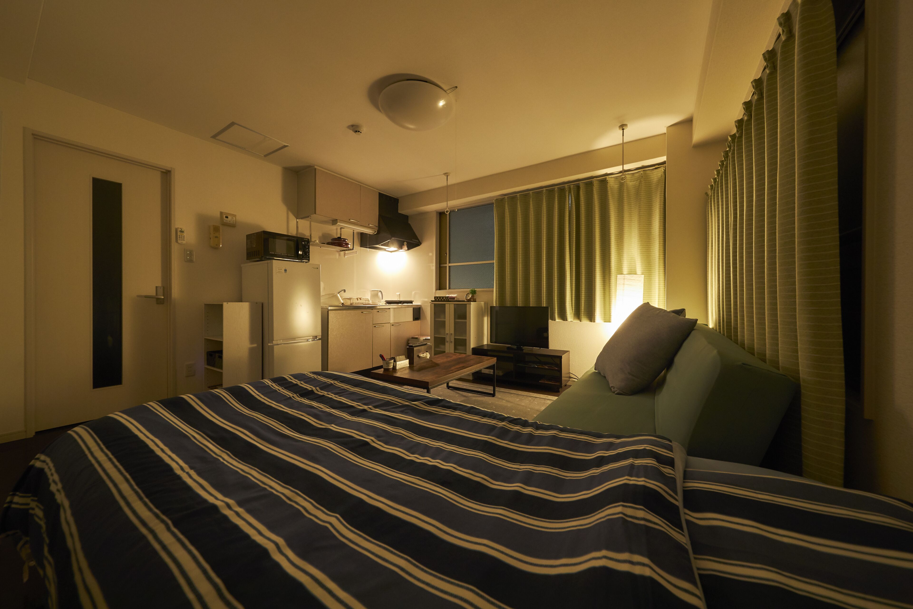 Habitación de hotel con cama, escritorio, silla, televisor y ventana con cortinas.