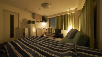 Habitación de hotel con cama, escritorio, silla, televisor y ventana con cortinas.