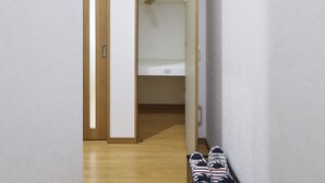Un pasillo con piso de madera, un zapatero y un armario con una cama.