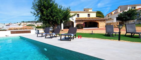 Piscina con sillones de descanso y un edificio de piedra al fondo.