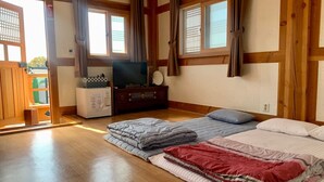 Ein Zimmer mit Holzboden, einem Bett mit vielen Kissen, einem Fernseher und einem kleinen Schrank.