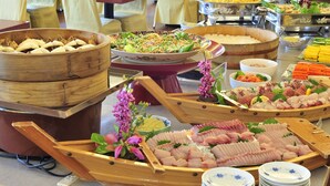 Ein Buffet mit verschiedenen Speisen, darunter Sushi, Gemüse und weitere Gerichte, anregend präsentiert auf Tischen und in Servierbehältern.