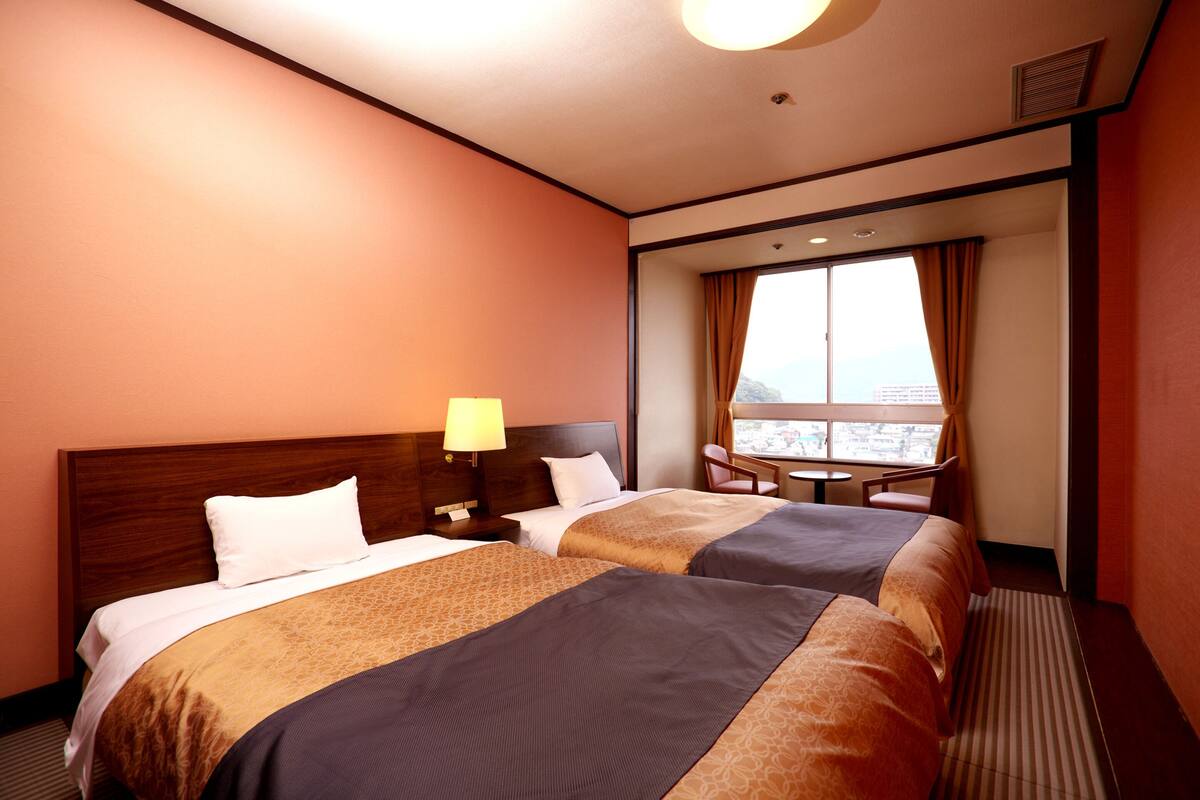 Une chambre d’hôtel avec deux lits, une petite table et une fenêtre avec des rideaux.