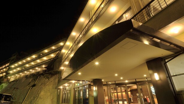 Ein mehrstöckiges Hotel mit modernem Design, das eine markante Treppe zum Eingang, große Fenster und eine gut beleuchtete Fassade zeigt.