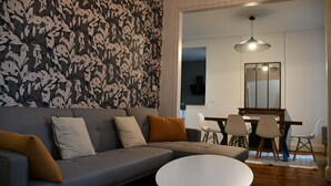 A modern living room with a grey sofa, white and brown cushions, a round white coffee table, and a dining area with a wooden table and chairs. - Maison bourgeoise Haussmannienne (Gîtes de France) (Limoges)