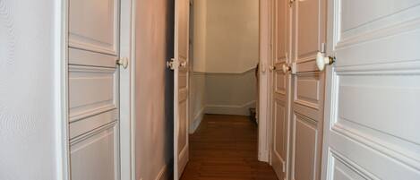 A narrow hallway with white doors and wooden flooring.