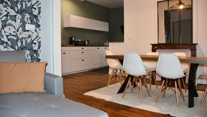 A modern living room with a grey sofa, a white rug, and a dining area with a wooden table and white chairs. - Maison bourgeoise Haussmannienne (Gîtes de France) (Limoges)