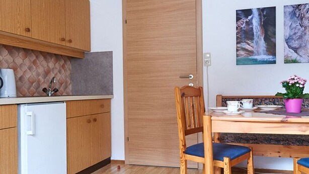 Una cocina compacta con armarios de madera, un refrigerador blanco, una mesa de comedor con sillas y una puerta.