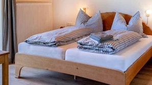 Parivuode, jossa on ruutukuviollinen vuodevaatteisto, puinen sängynrunko ja yöpöytävalaisimet.