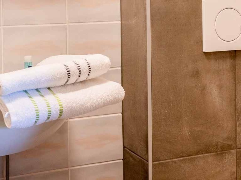 A bathroom with a towel rack holding two towels, a soap dispenser, and a wall-mounted thermostat.