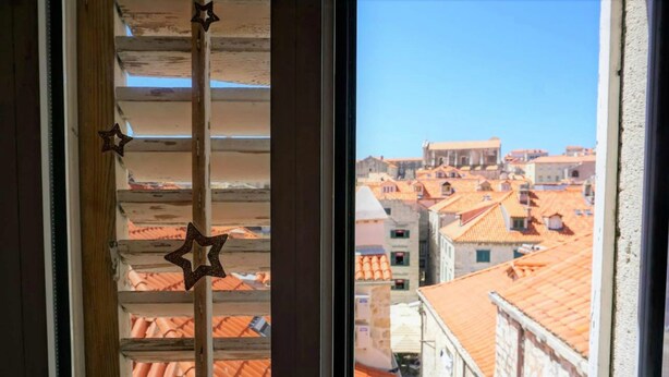Vista a través de una ventana con adornos de estrellas, mostrando un paisaje urbano con edificios de tejados de teja.