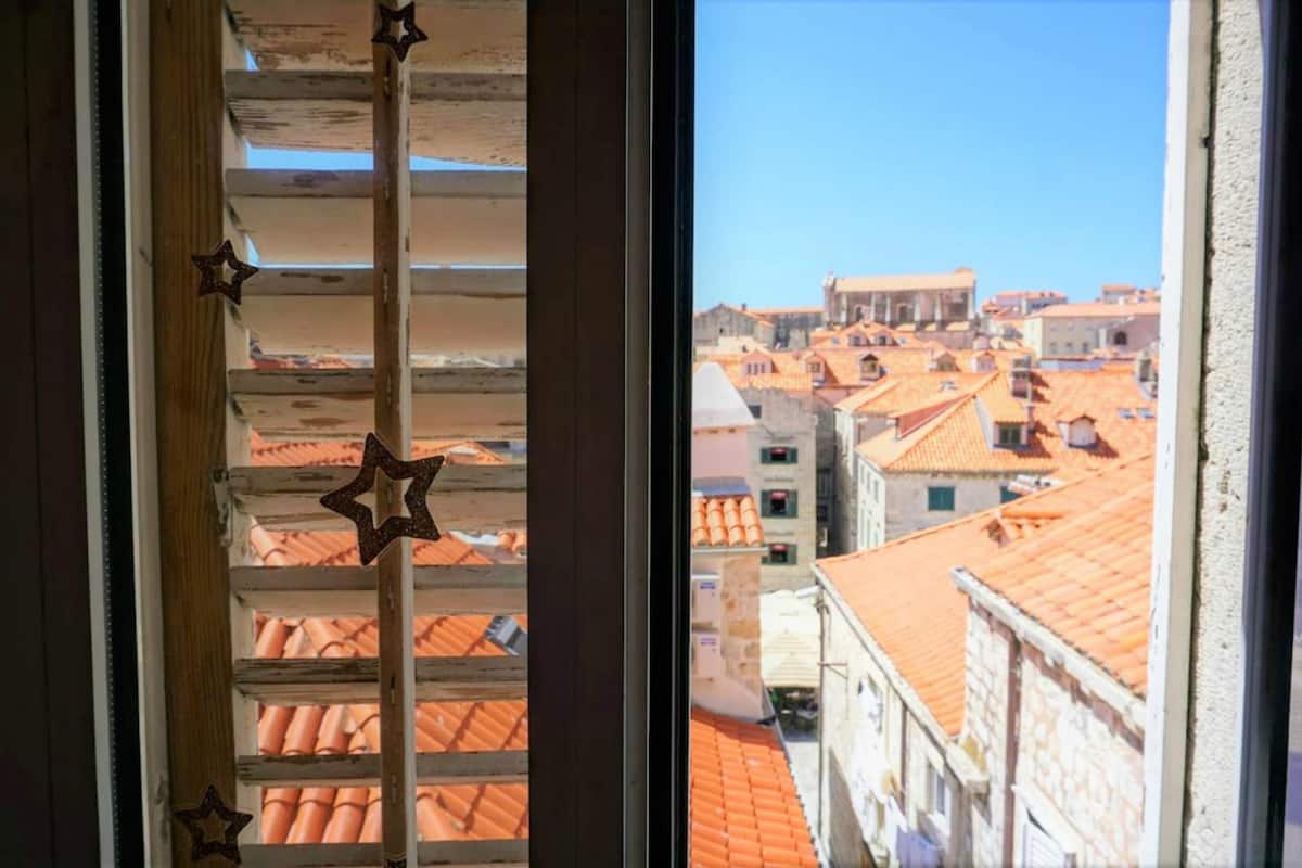 Blick durch ein Fenster mit Sterndekorationen auf eine Stadtansicht mit Häusern mit Terrakotta-Dächern.