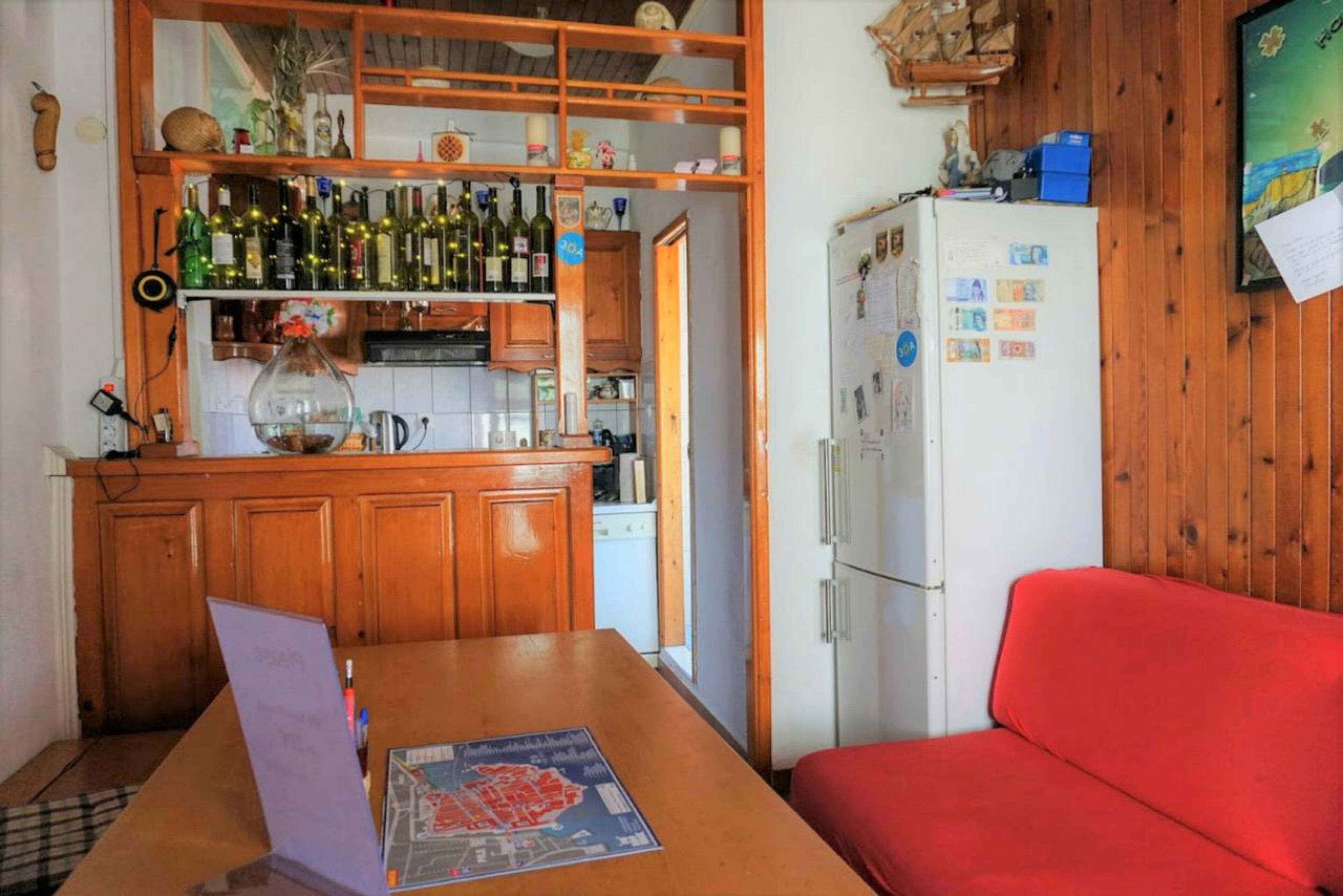 A compact kitchen with wooden cabinets, a refrigerator, and a dining table with a map.