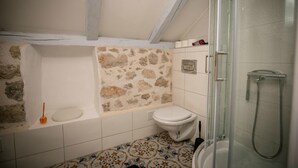 A bathroom with a stone wall, a toilet, a bathtub, and a glass-enclosed shower. - Rooms Epidaurus (Dubrovnik)