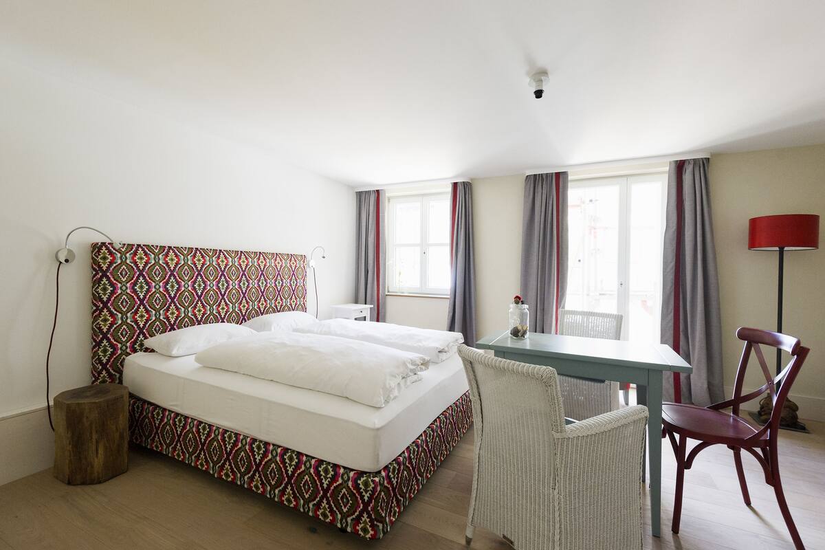 Un dormitorio con una cama estampada, un escritorio y dos sillas.