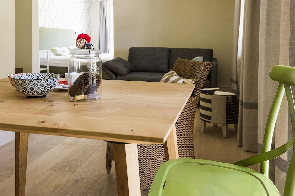 Un comedor con una mesa de madera, una silla verde, un frasco con piñas y un cuenco estampado.