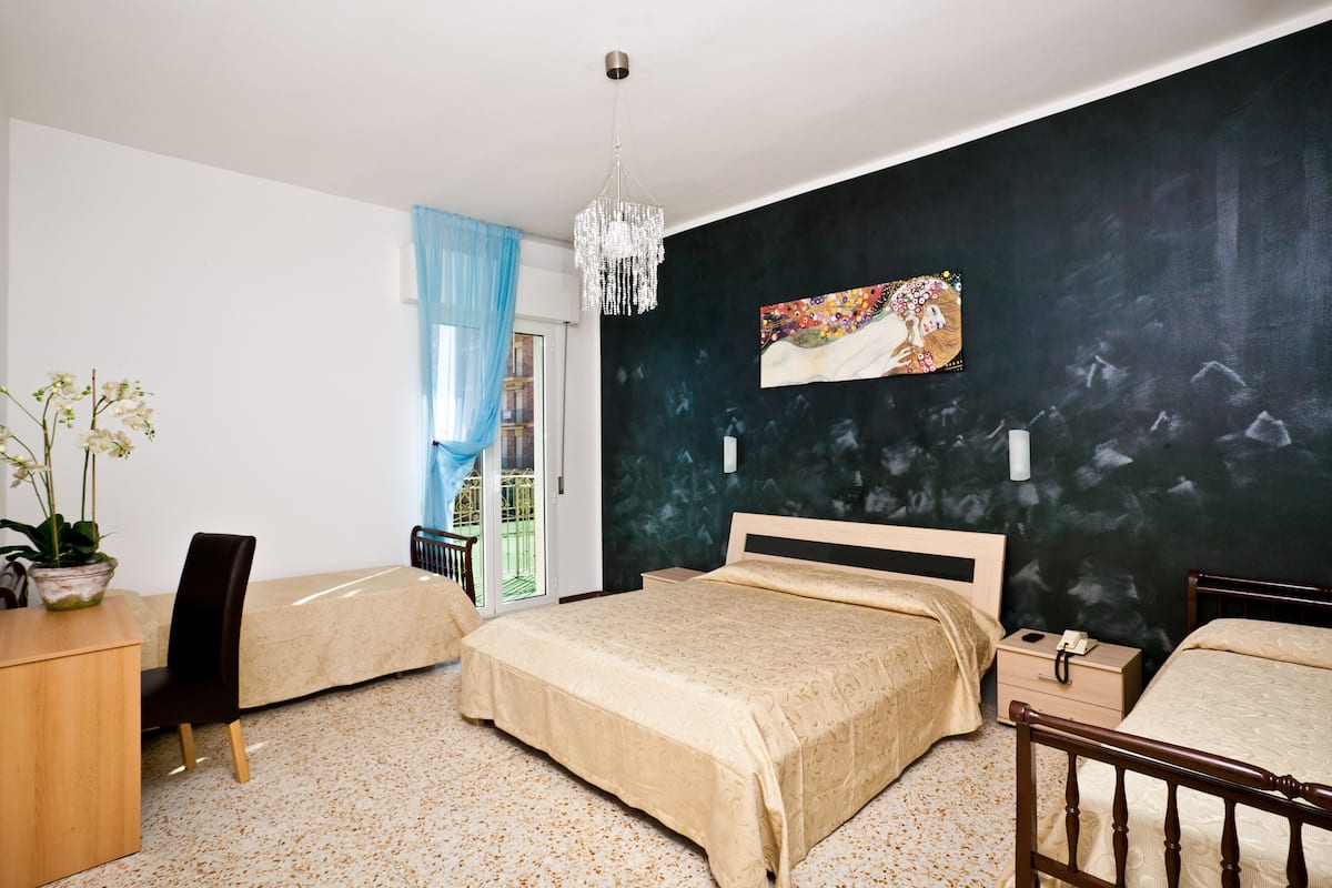 Habitación de hotel con dos camas, un escritorio, una silla, una planta en maceta, una araña y un cuadro en la pared.
