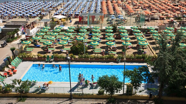 Una gran piscina rodeada de numerosas sombrillas y tumbonas.