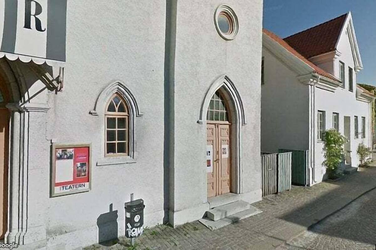 A building with arched windows and a door, a trash bin, and a sign that reads "TEATERN".