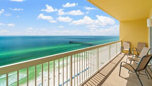 Un balcon avec vue sur l’océan et la plage, offrant un panorama sur une jetée et des chaises de plage.