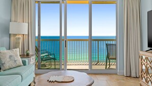Une chambre avec vue sur l’océan, un balcon avec des chaises, une télévision et une table agrémentée d’un objet décoratif.