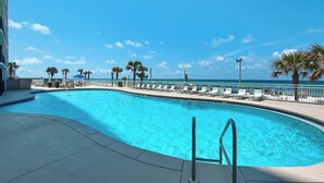 A swimming pool with a view of the ocean, surrounded by lounge chairs and palm trees. - Watercrest 1005 (Panama City Beach)