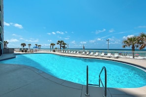 A swimming pool with a view of the ocean, surrounded by lounge chairs and palm trees. - Watercrest 1005 (Panama City Beach)