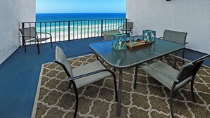 A balcony with a glass table, chairs, and a view of the ocean. - Watercrest 1005 (Panama City Beach)